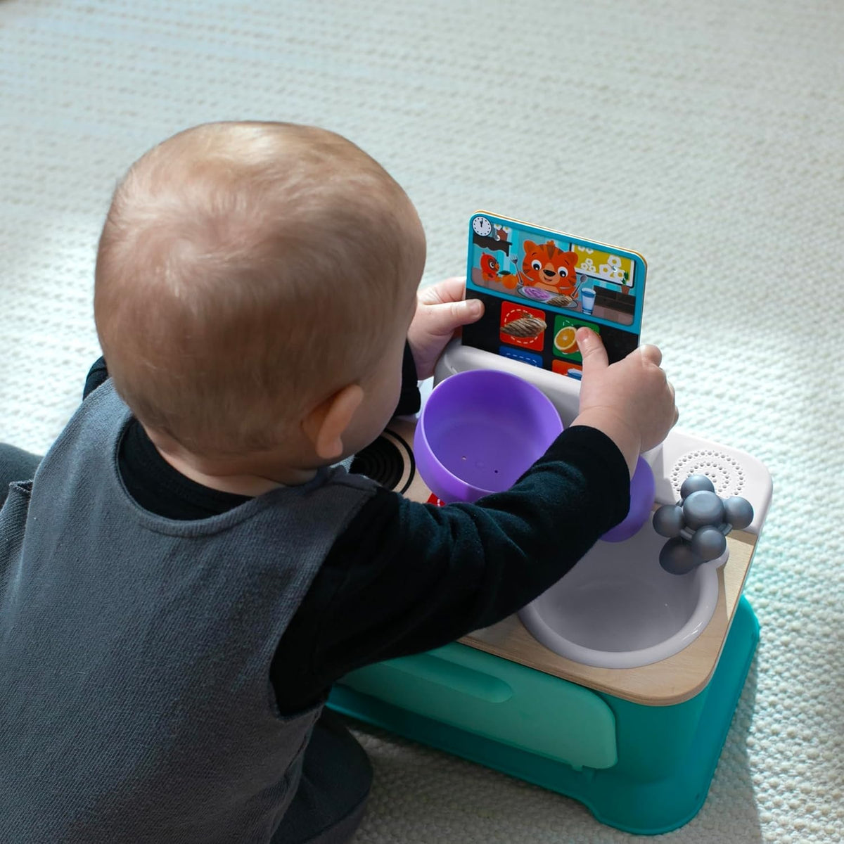 Dziecko bawiące się fioletowym garnkiem przy kuchni Baby Einstein Hape.